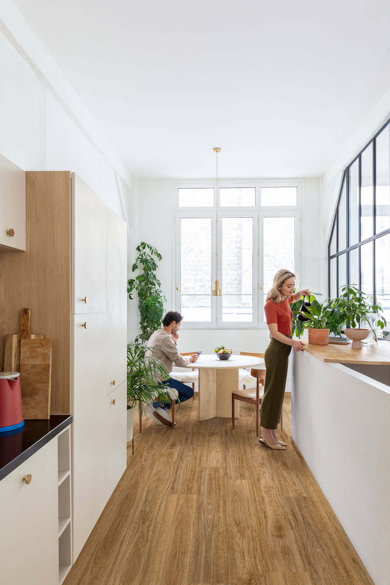 Modern kitchen with wooden floor and white walls, featuring two people.