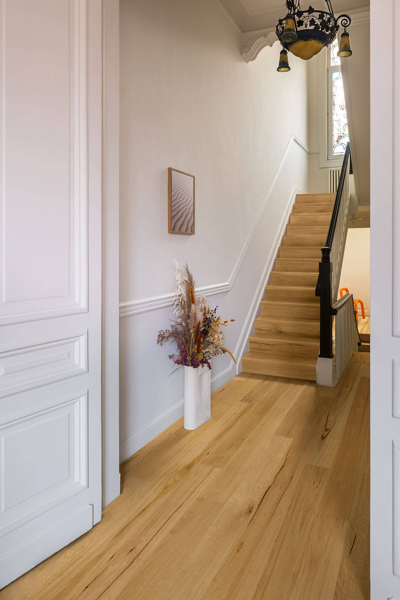 Staircase with wooden floor and white walls, featuring a vase with dried flowers.