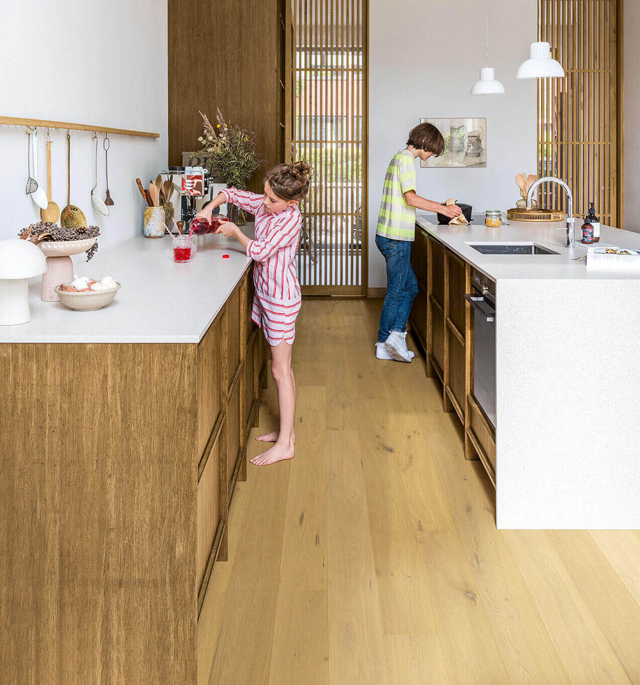 Two children in a modern kitchen with wooden floors and white countertops.