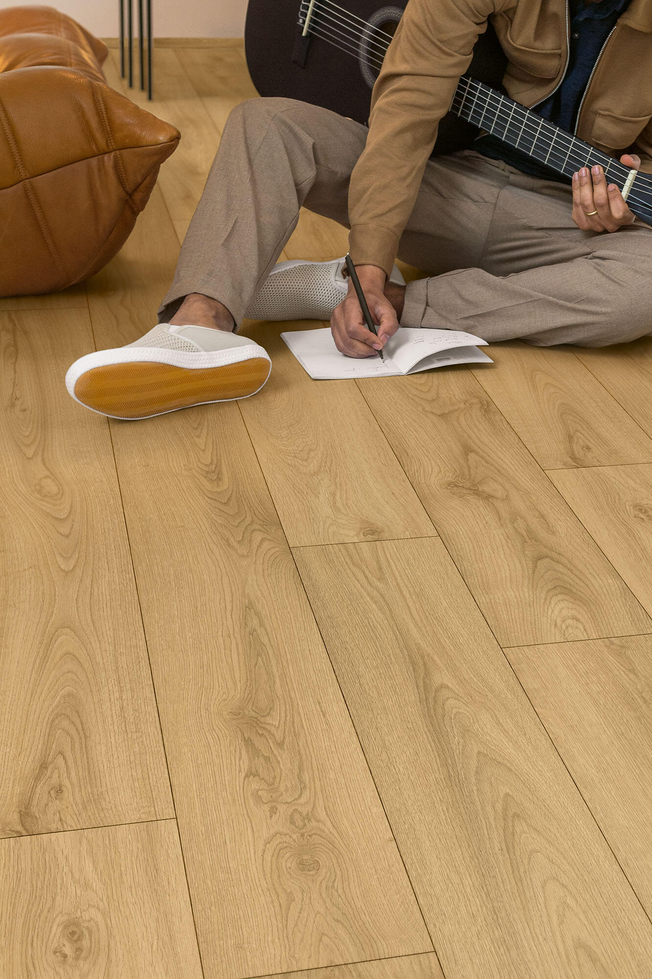 Person playing guitar and writing in a notebook on a wooden floor