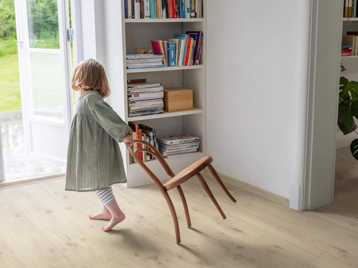 Child playing with a wooden chair in a room with bookshelves.
