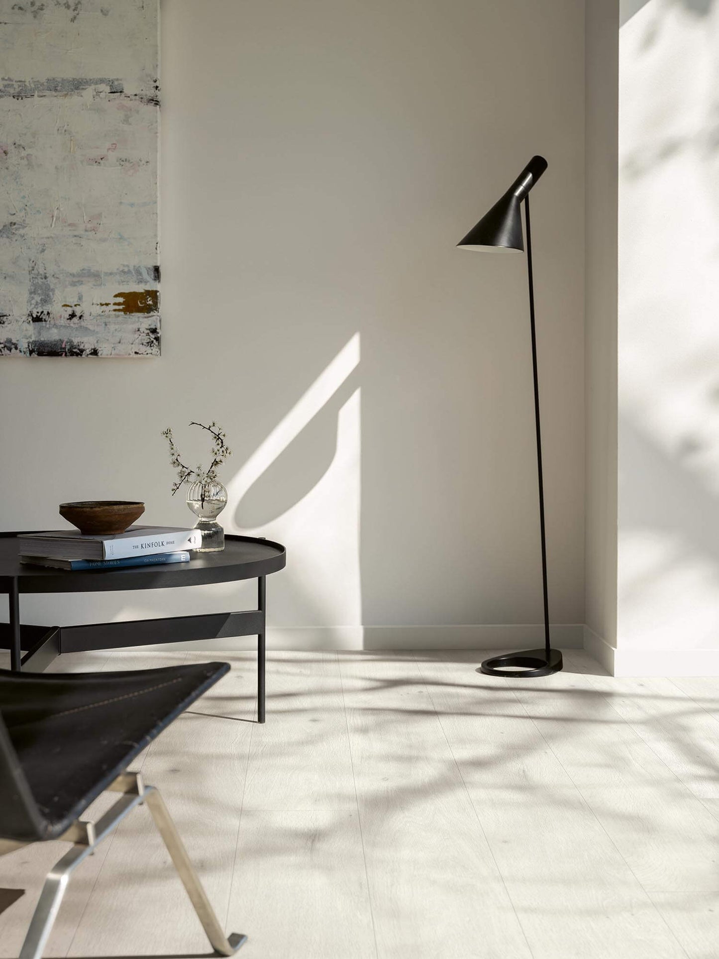 Modern black floor lamp next to a small table with decor items in a minimalistic room.