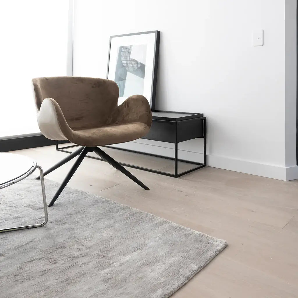 Modern brown chair in a minimalistic room with a rug and side table.