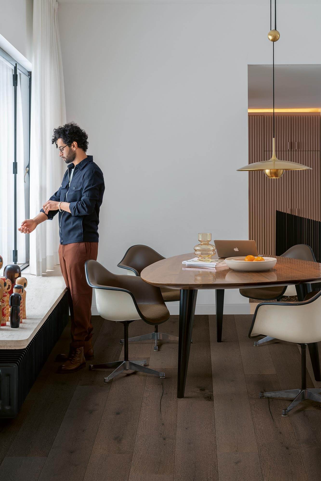 Man standing by a window in a modern dining room with a table and chairs.