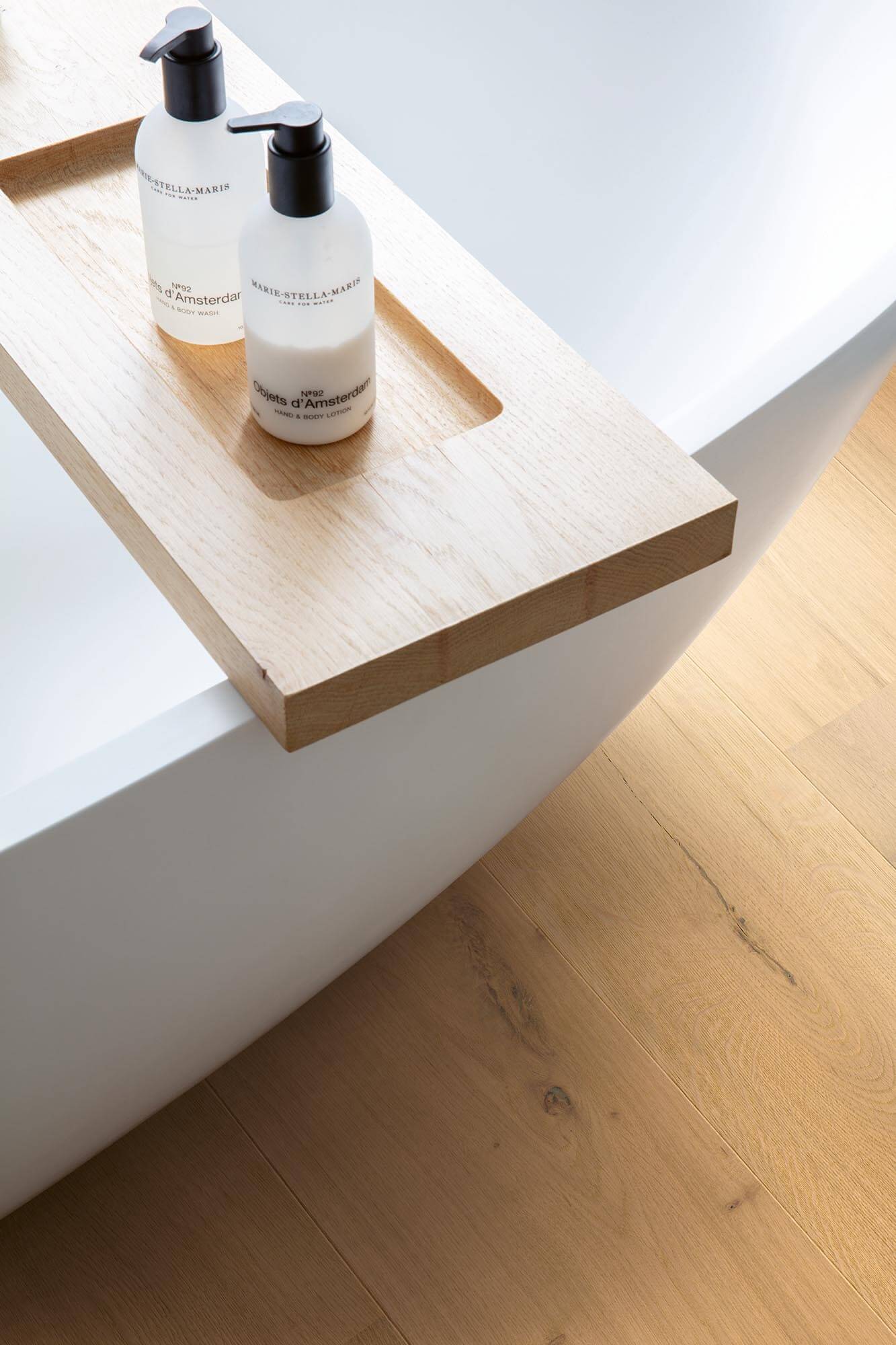 Two bottles of shampoo on a wooden tray next to a white bathtub.