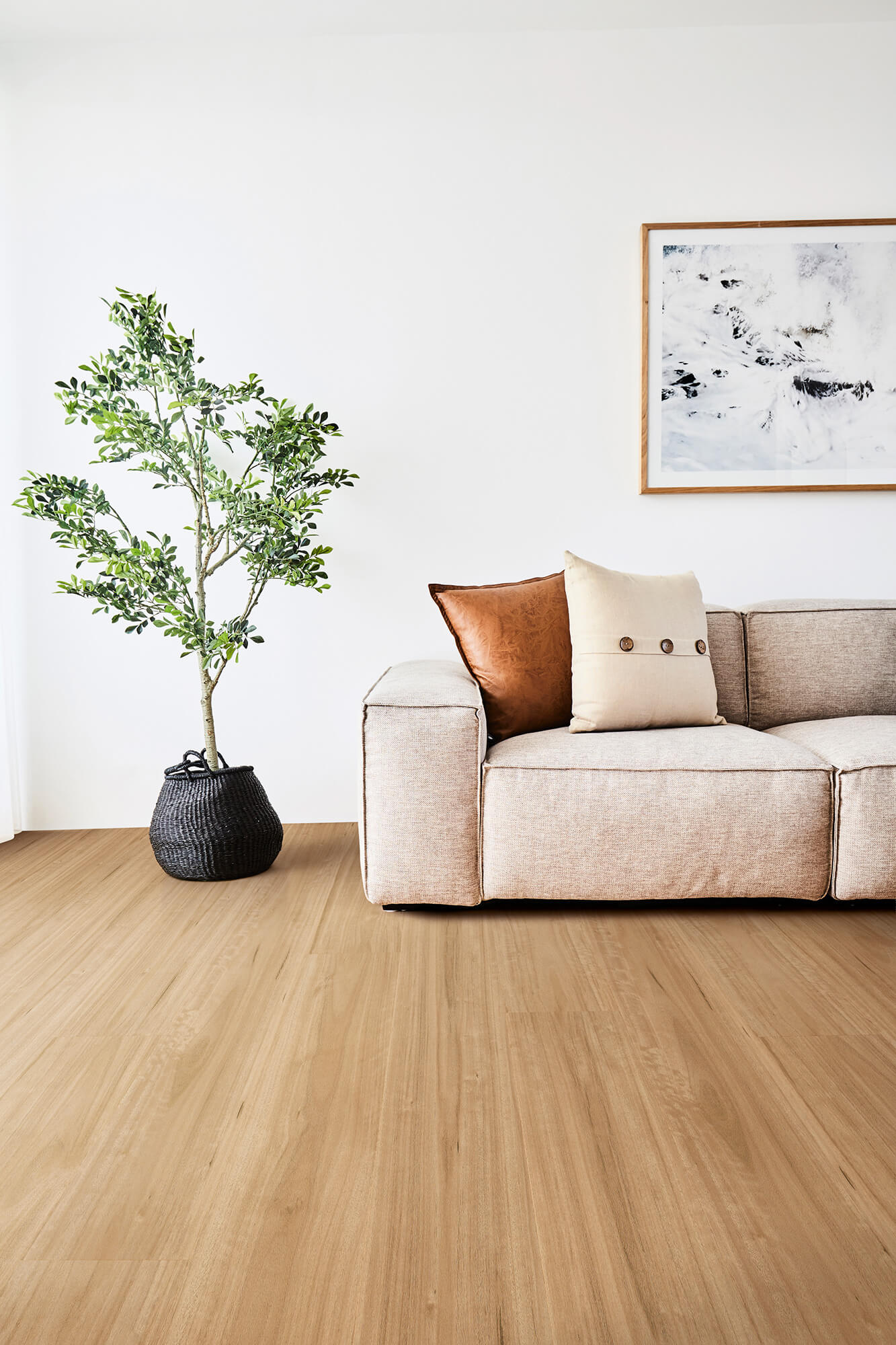 Beige sofa with decorative pillows and a plant on a wooden floor in a minimalistic living room.