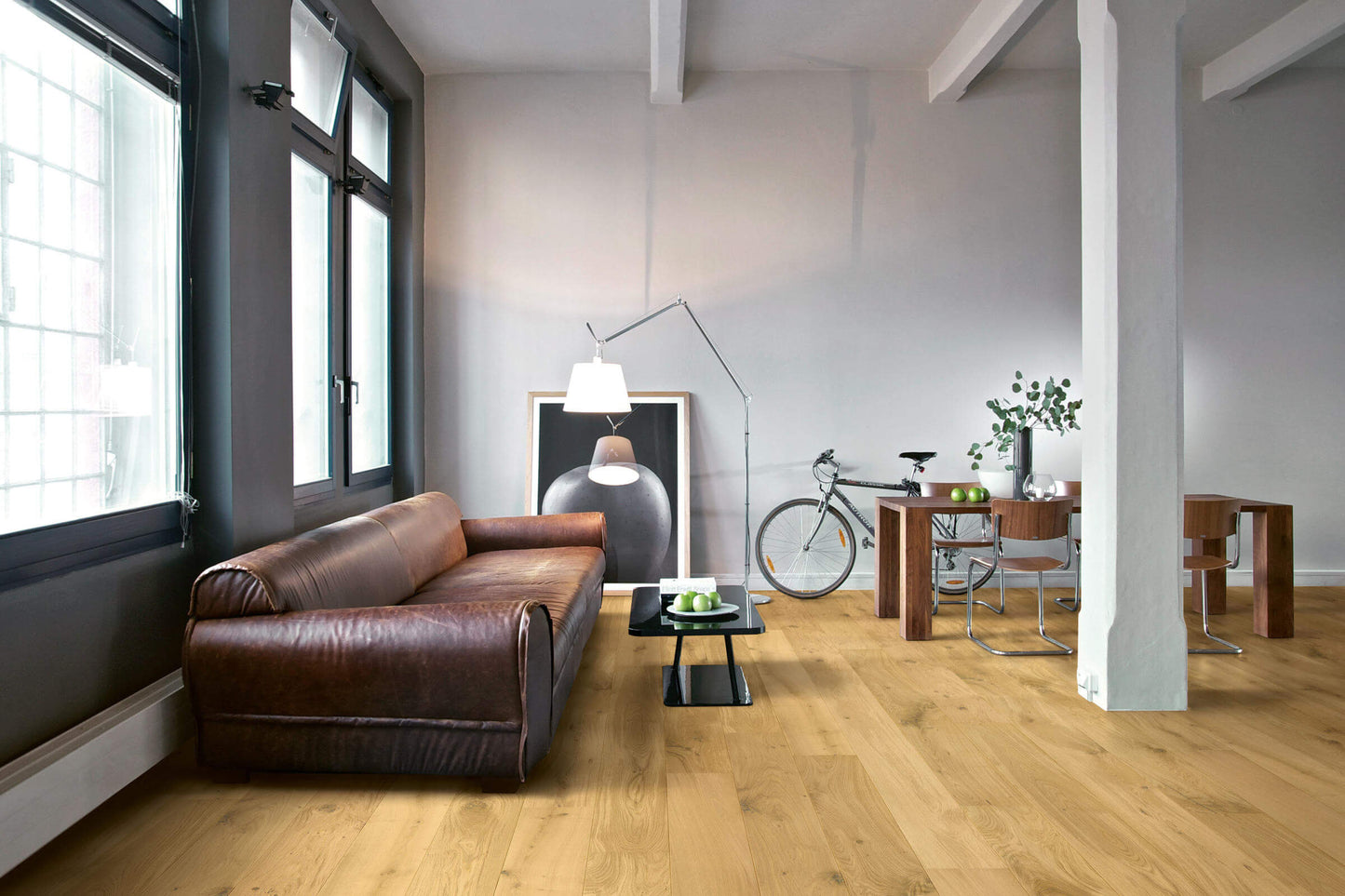 Modern living room with a brown leather sofa, wooden floor, and large windows.
