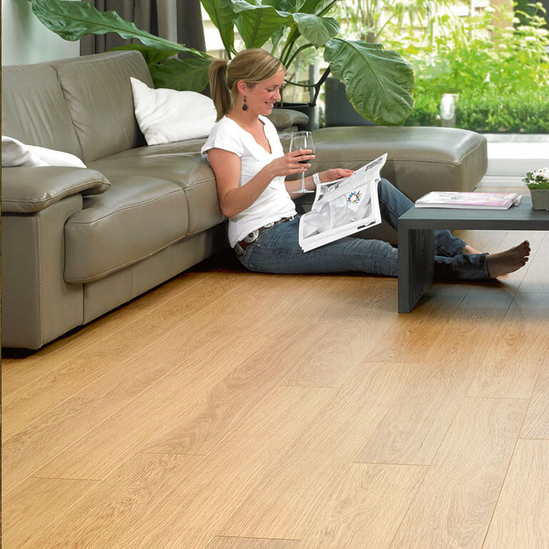 Woman sitting on a couch reading a newspaper in a living room with wooden flooring.
