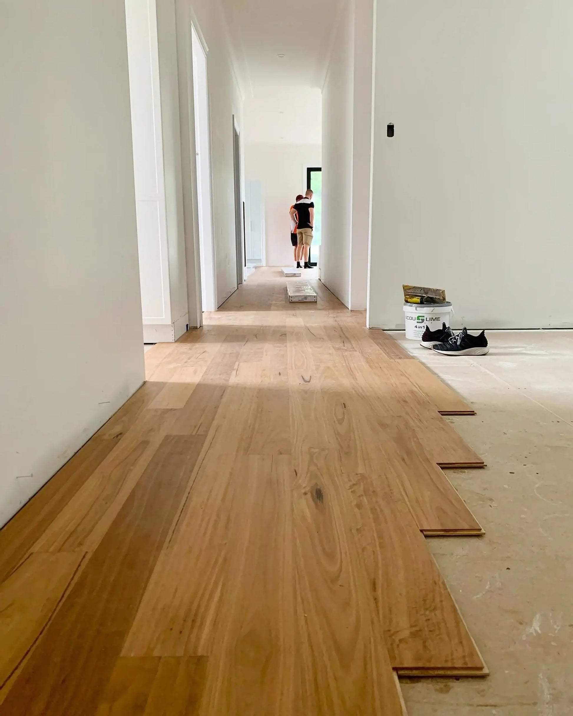Wooden flooring installation in a room with white walls and a person in the background.