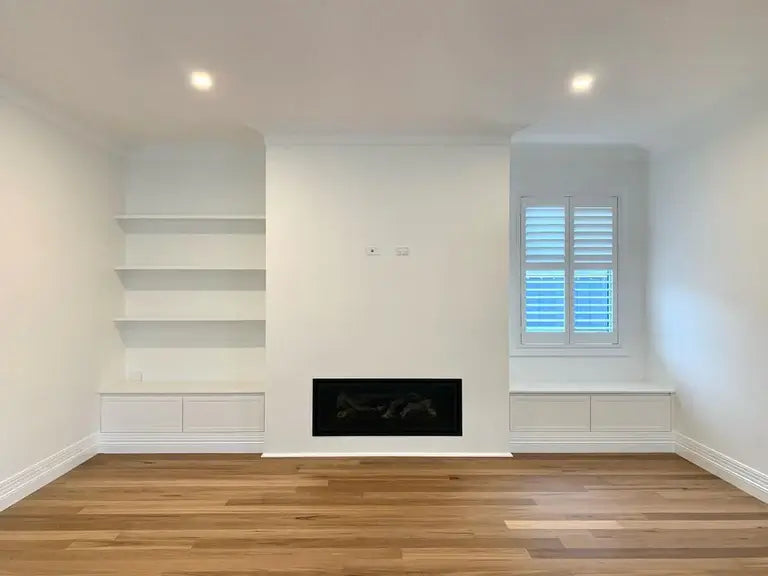 Empty room with white walls, wooden floor, and a fireplace.
