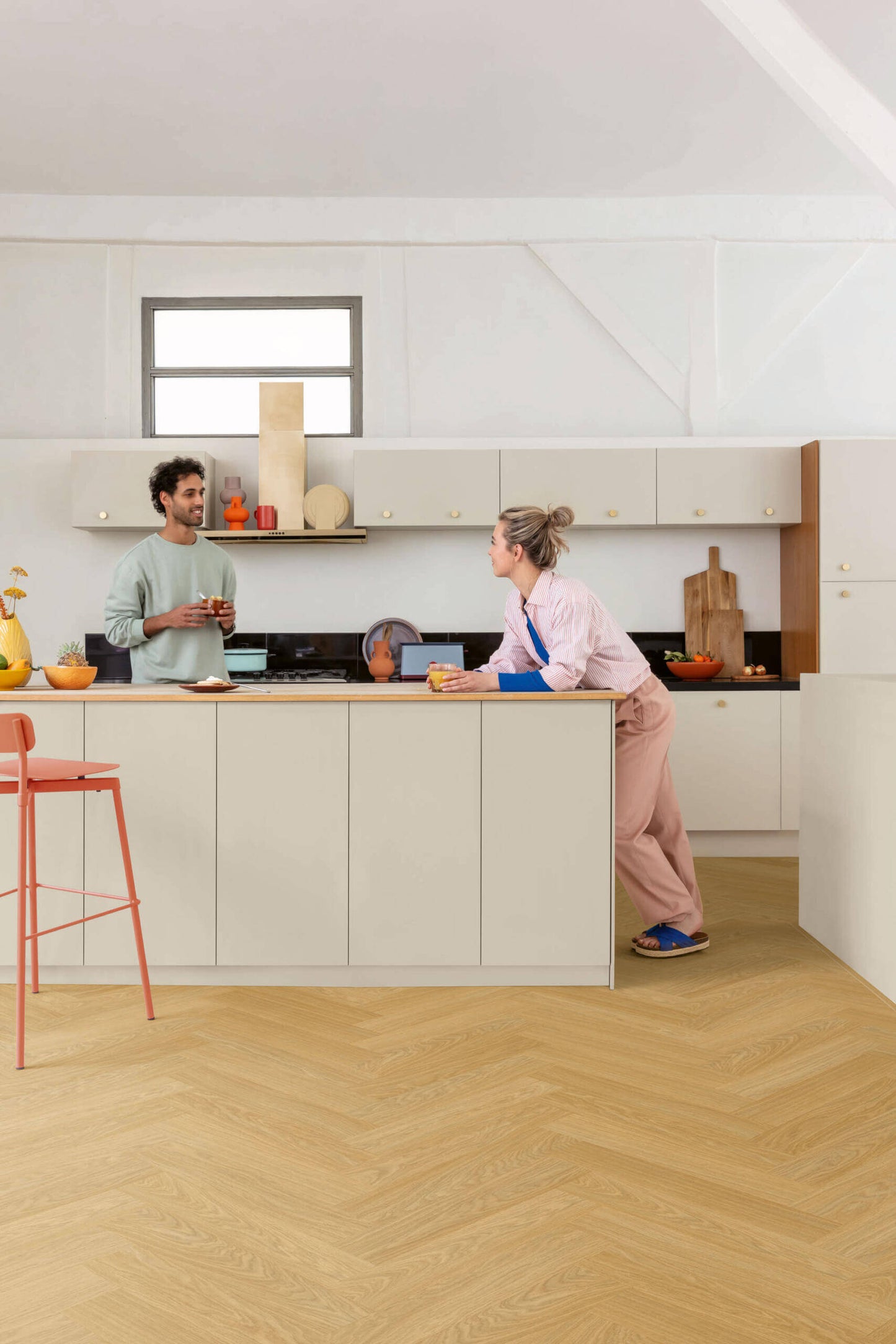 Two people in a modern kitchen with light-colored cabinets and wooden flooring.