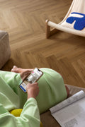 Person sitting on a wooden floor using a smartphone with a magazine open nearby.
