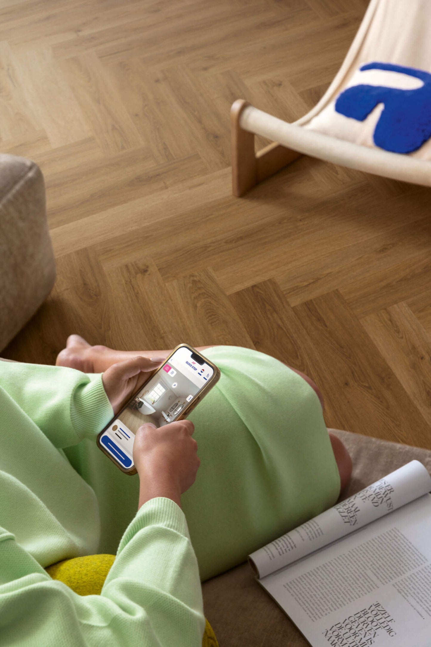 Person sitting on a wooden floor using a smartphone with a magazine open nearby.