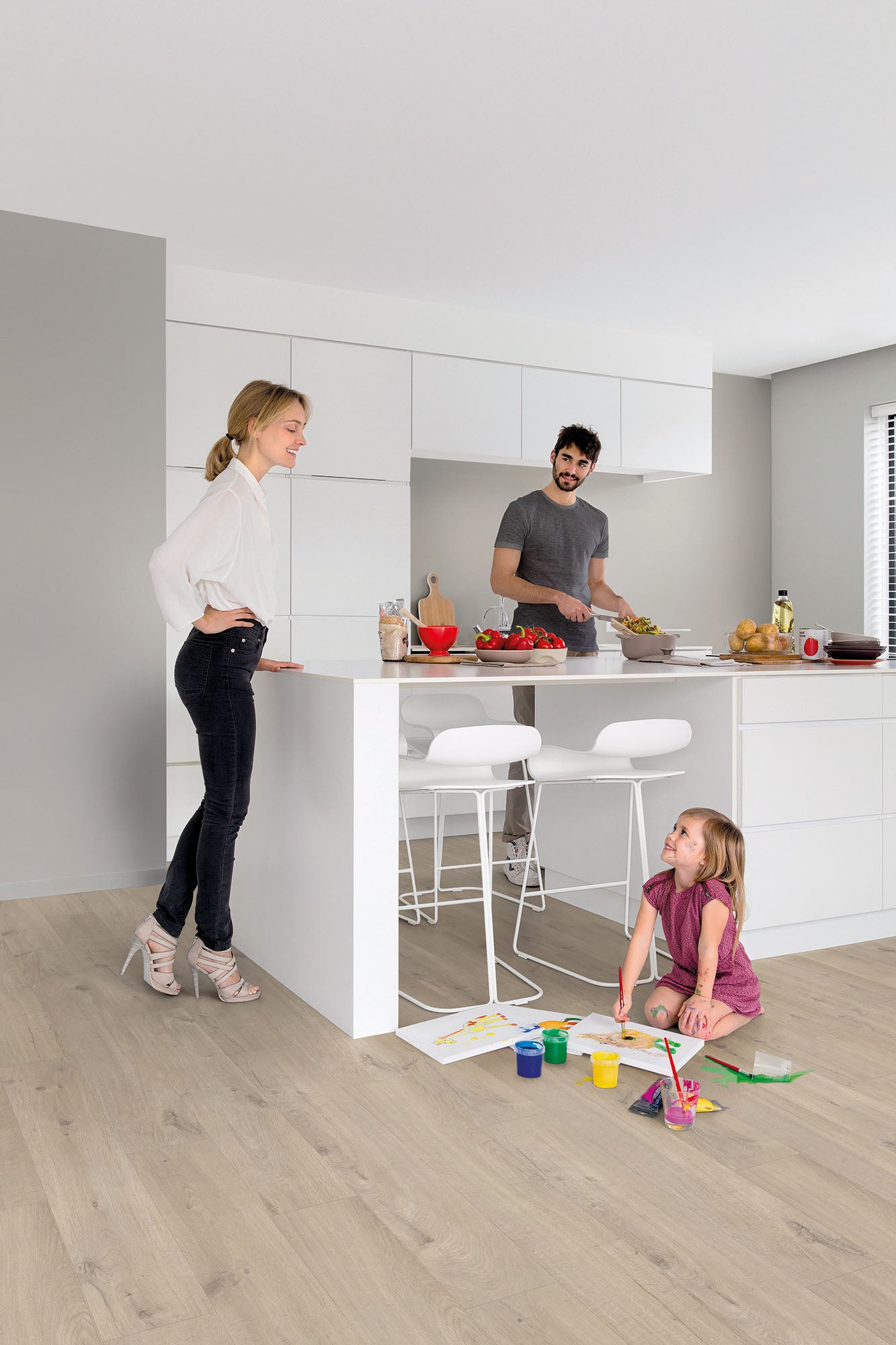 Family in a modern kitchen with white cabinets and wooden flooring.