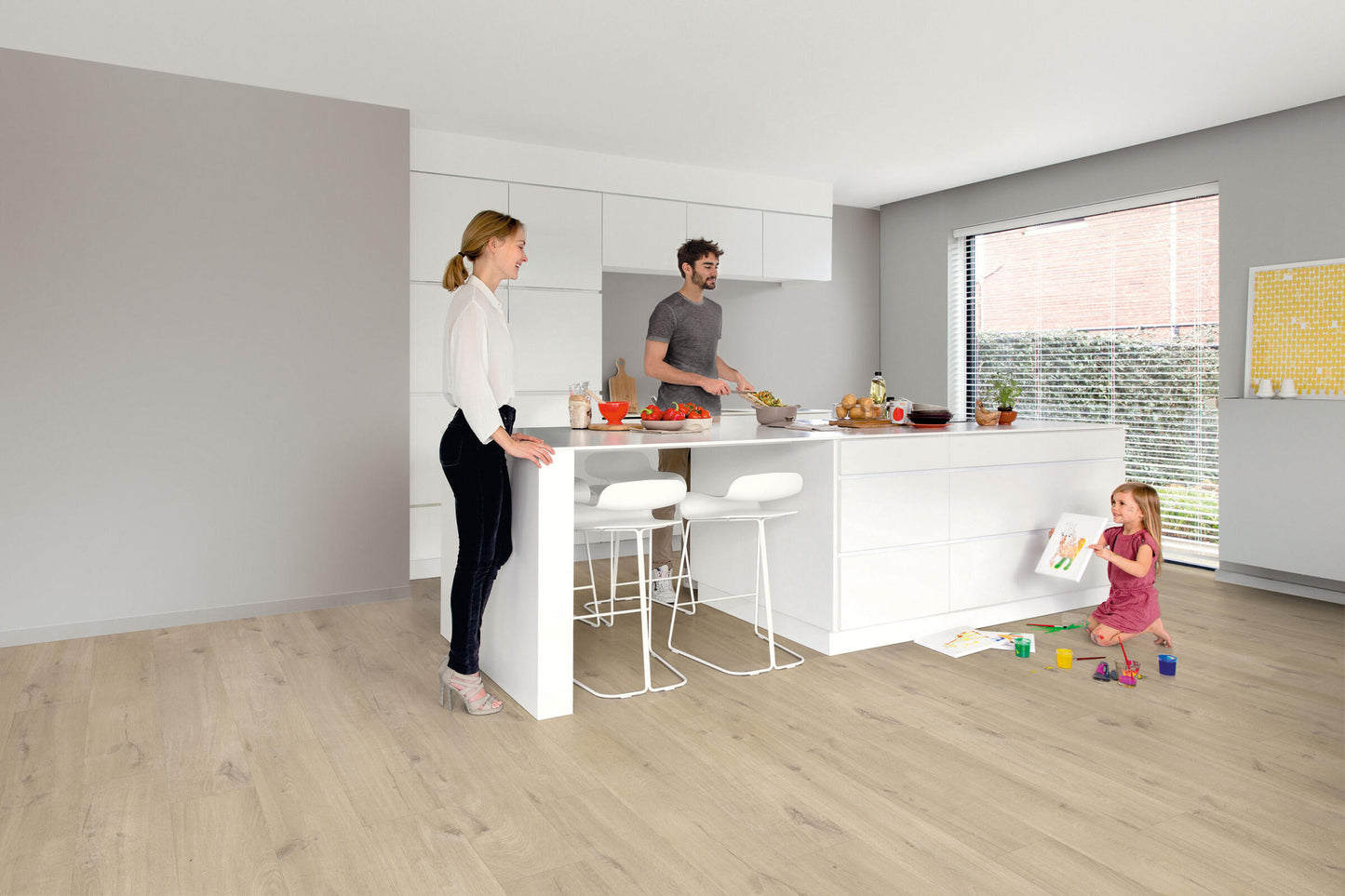Family in a modern kitchen with white countertops and light wood flooring.