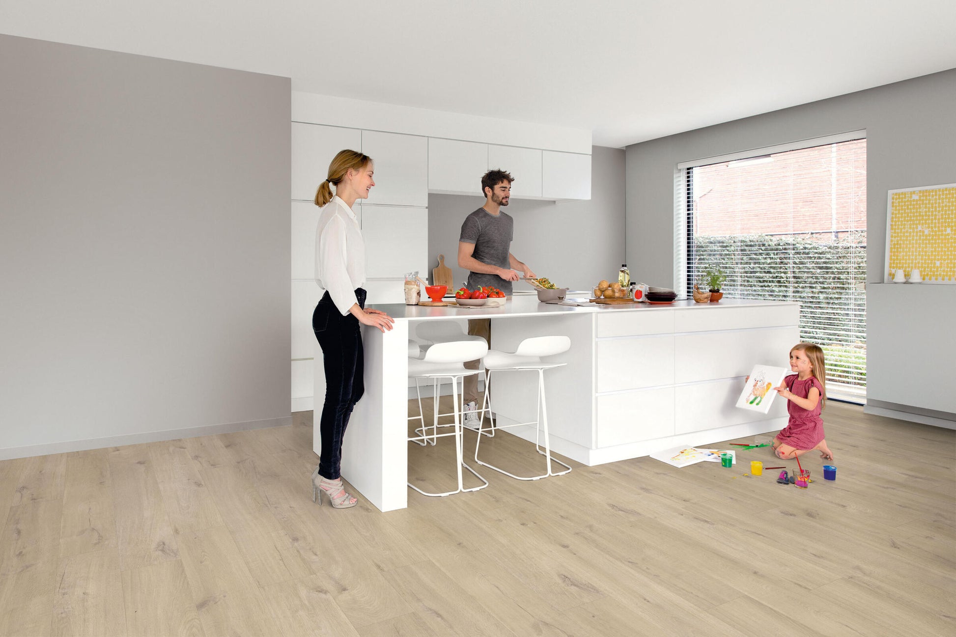 Family in a modern kitchen with white countertops and light wood flooring.