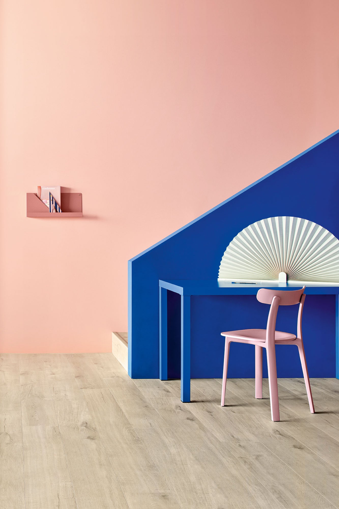 Modern interior with pink chair, blue wall, and white decorative fan.