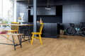 Modern kitchen with black cabinets, wooden floor, and yellow chairs.
