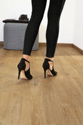 Person wearing black high-heeled shoes on a wooden floor