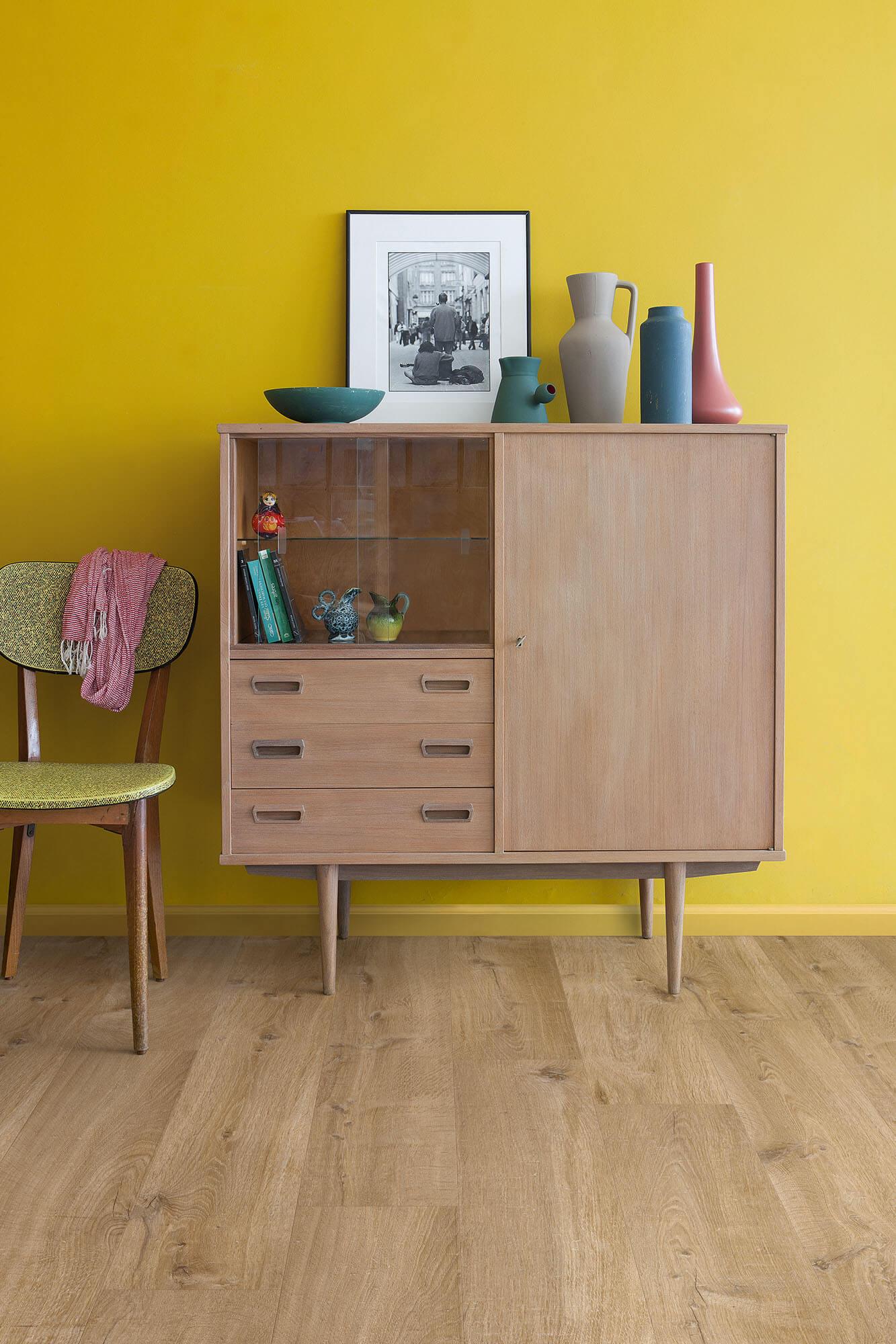 Wooden cabinet with open door displaying decorative items against a yellow wall.