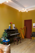 Room with a piano, harp, and decorative items against a yellow wall.