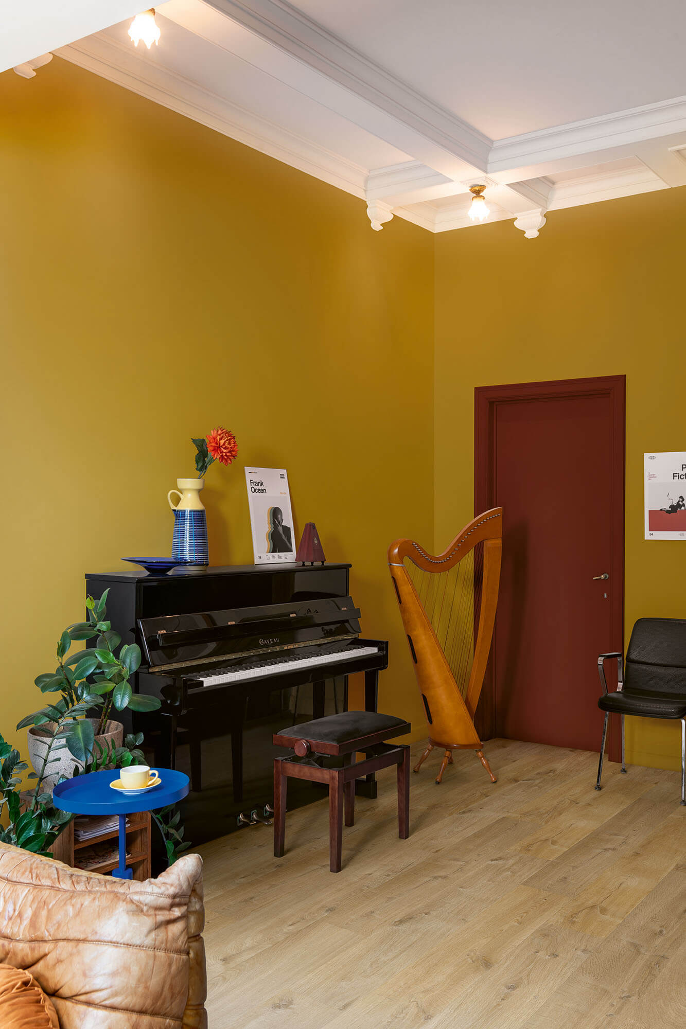 Room with a piano, harp, and decorative items against a yellow wall.