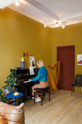 Person playing a piano in a room with yellow walls, a harp, and a door.