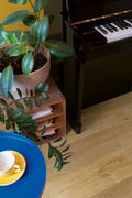 Piano with a plant and a table with a cup and saucer in a room.