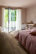 Modern bedroom with pink bedding, wooden floor, and large glass door leading to outdoor area.