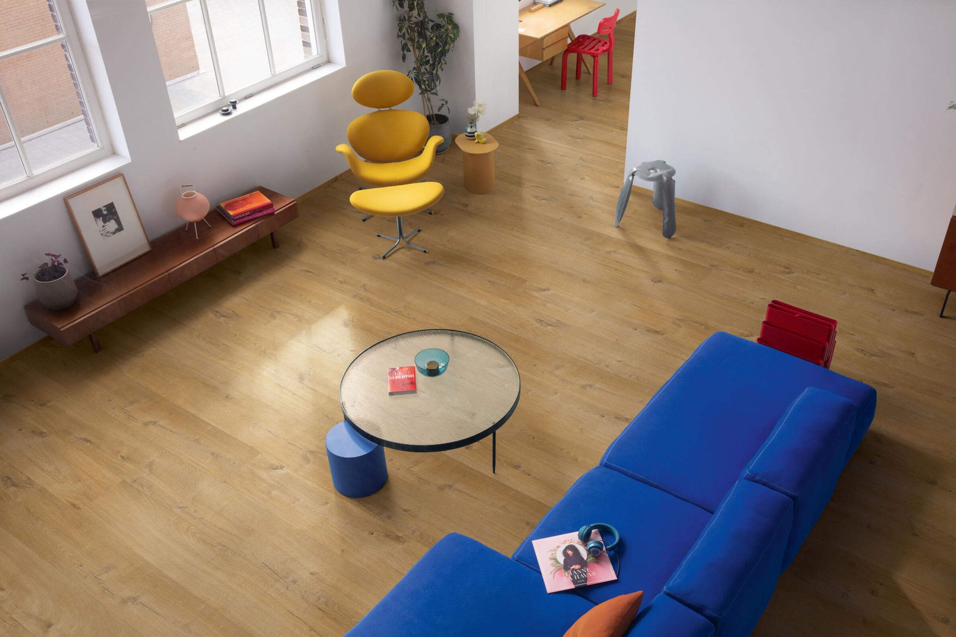Modern living room with blue sofa, yellow chairs, and a round glass table.