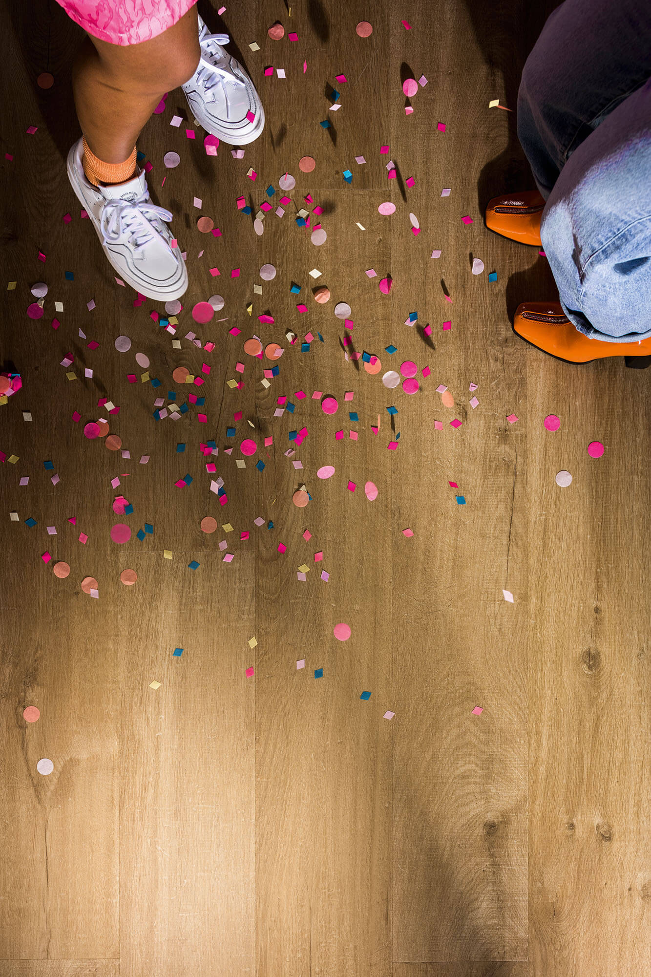 Two people standing on a wooden floor with colorful confetti scattered around them.