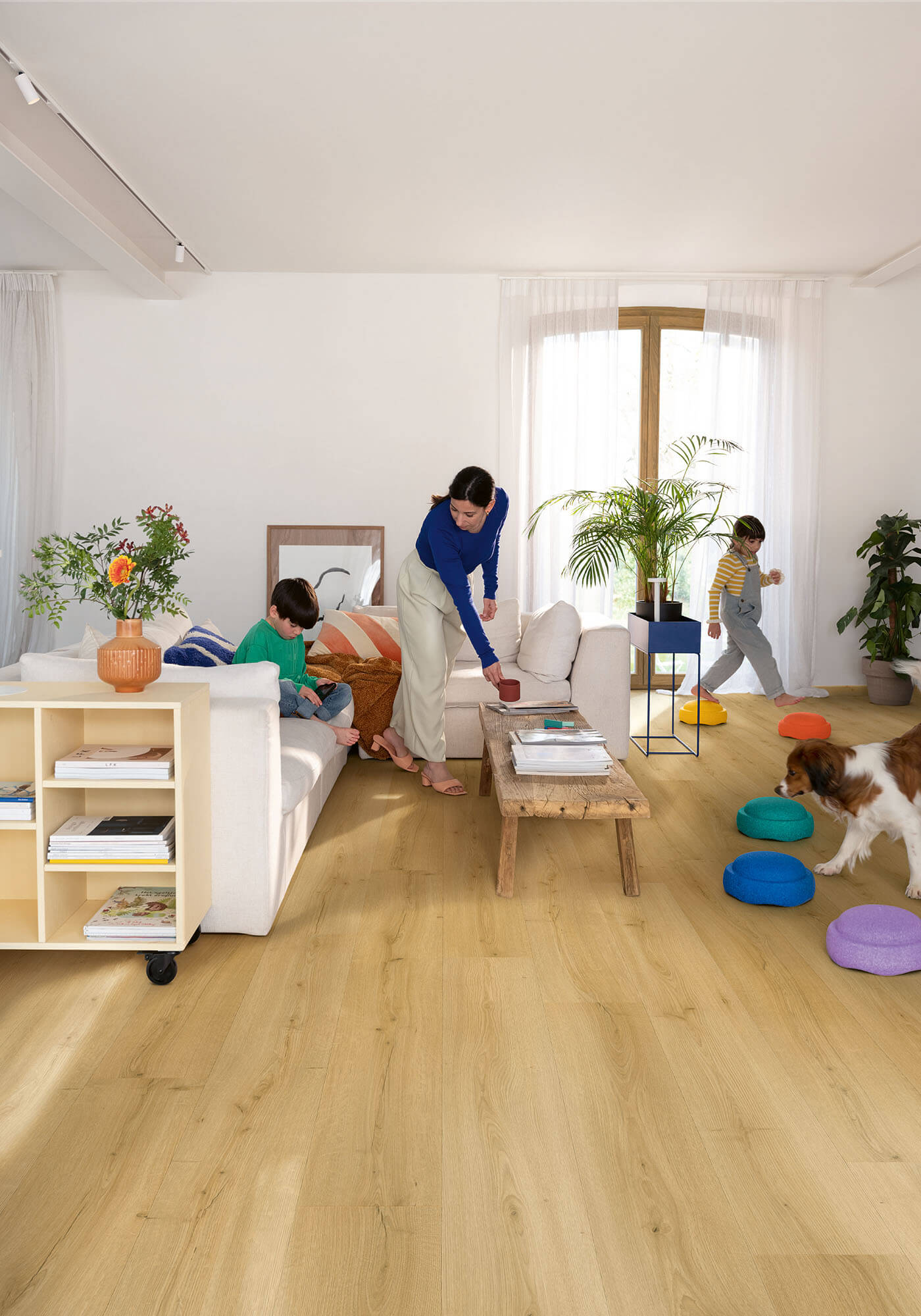 Living room with wooden flooring, white walls, and people interacting.