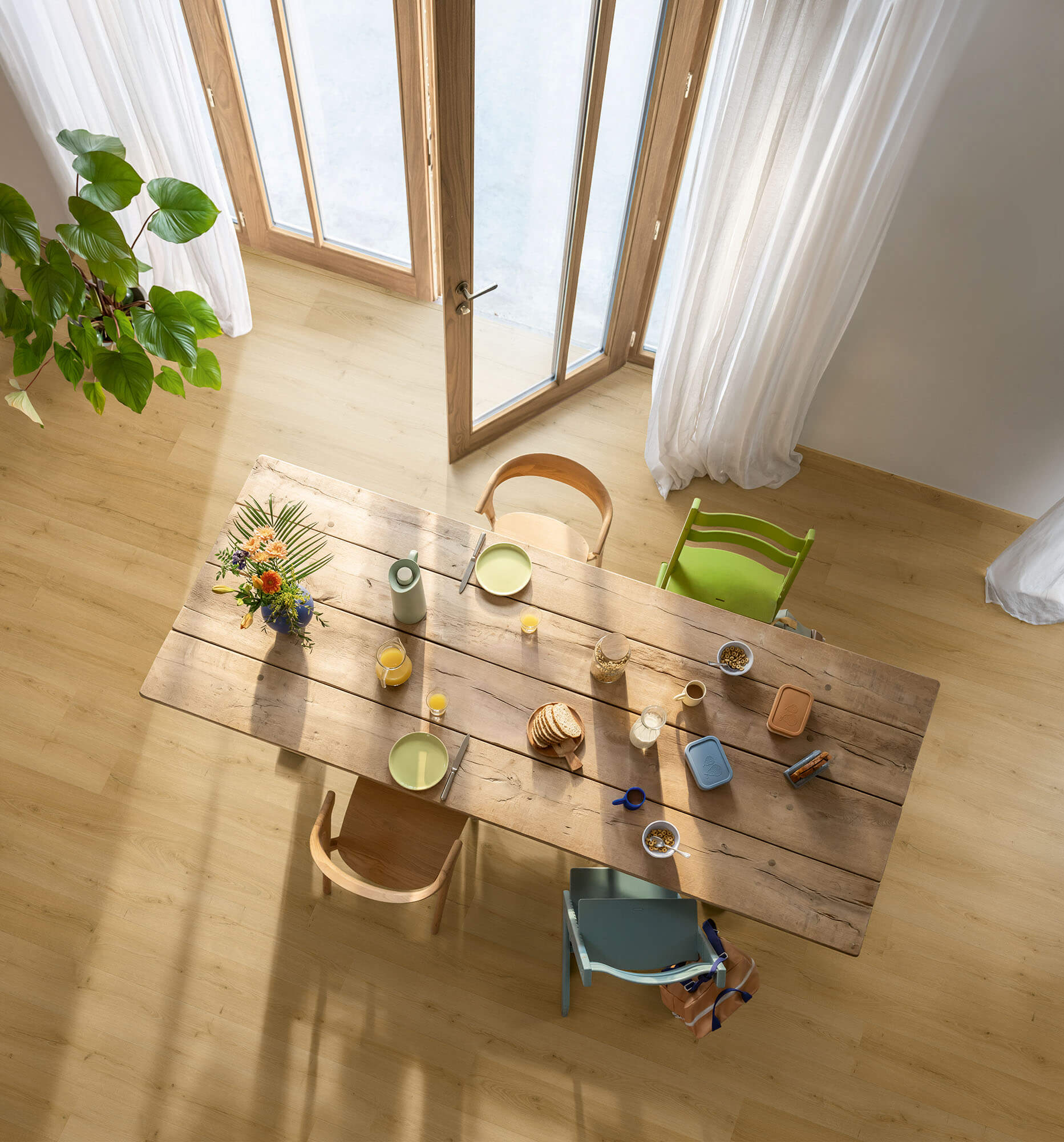 Dining area with a wooden table and chairs in a bright room with large windows.