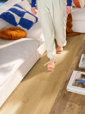 Person walking on a wooden floor in a living room with a couch and pillows.