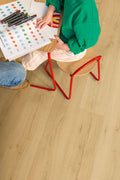 Person sitting at a table with a coloring book and markers on a wooden floor.