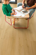 Two children sitting at a small table with coloring books and crayons on a wooden floor.