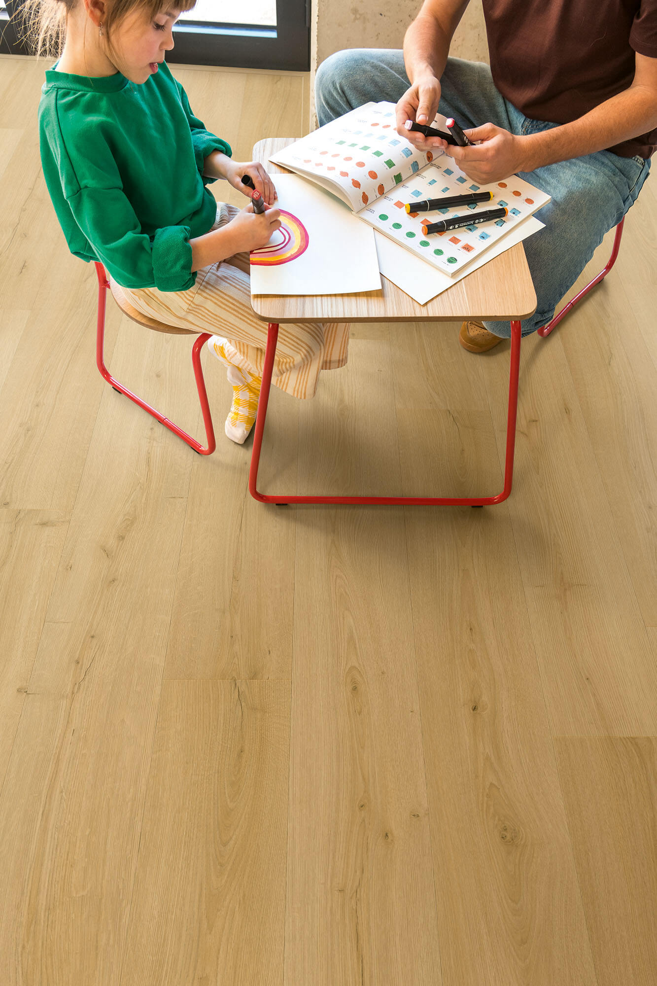 Two children sitting at a small table with coloring books and crayons on a wooden floor.