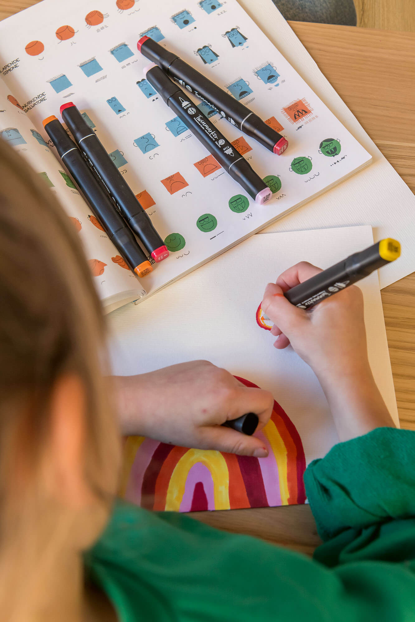 Child coloring a rainbow with markers on a worksheet