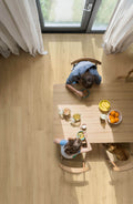 Two children sitting at a wooden table with snacks in a bright room.