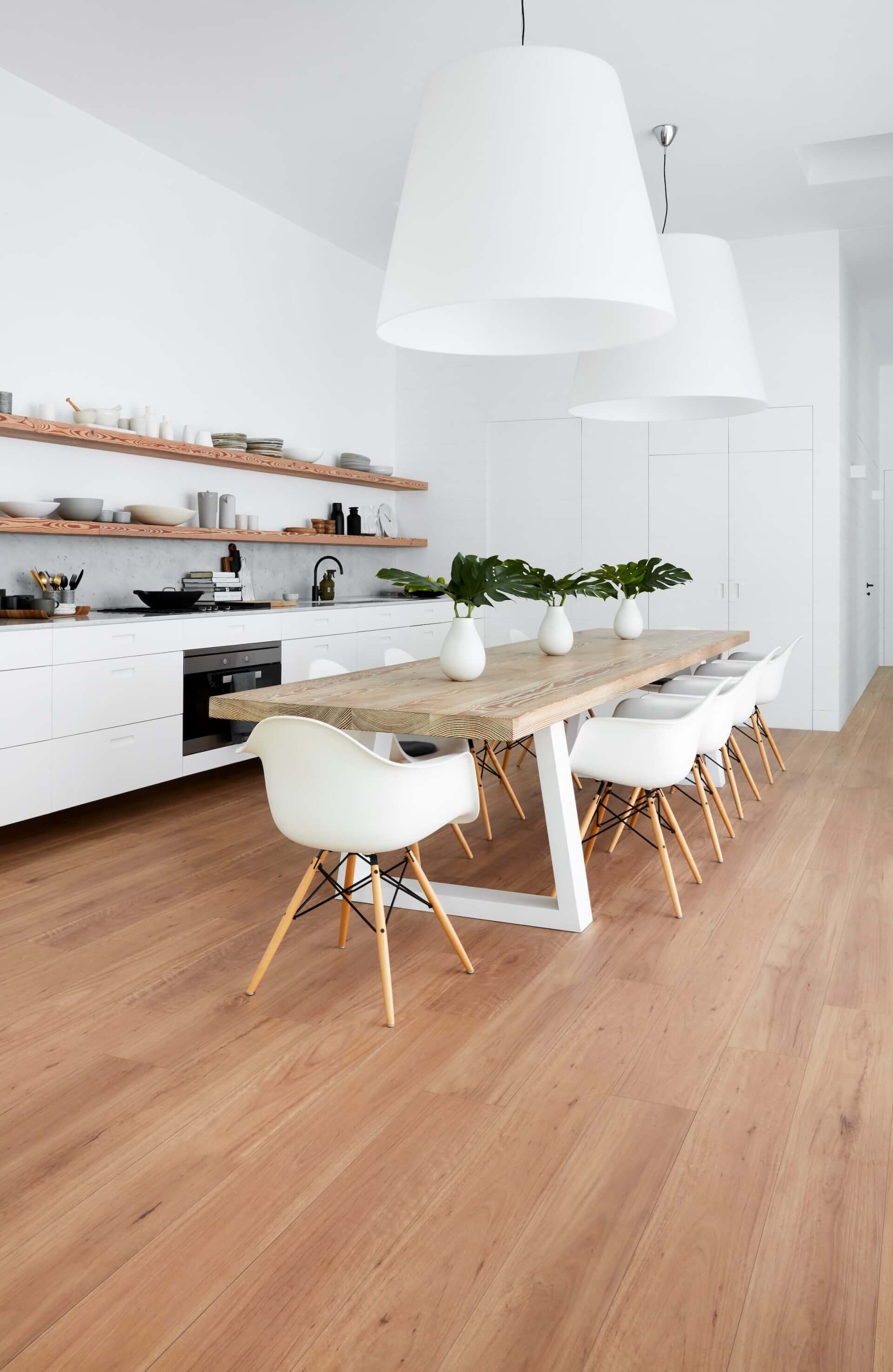 Modern kitchen with wooden dining table and chairs, white pendant lights, and open shelves.