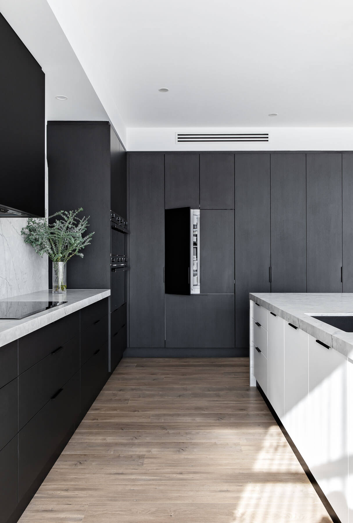 Modern kitchen with black and white cabinetry, wooden floor, and white ceiling.