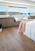 Modern bedroom with wooden floor, bed with pink blanket, and large windows overlooking a coastal view.