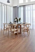 Dining room with wooden table and chairs, large windows, and a vase of flowers.