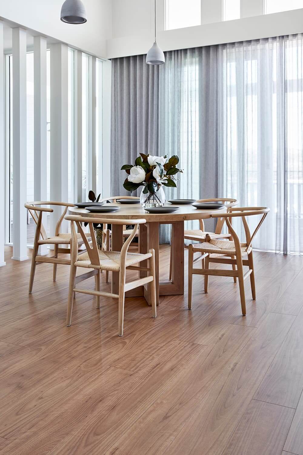 Dining room with wooden table and chairs, large windows, and a vase of flowers.