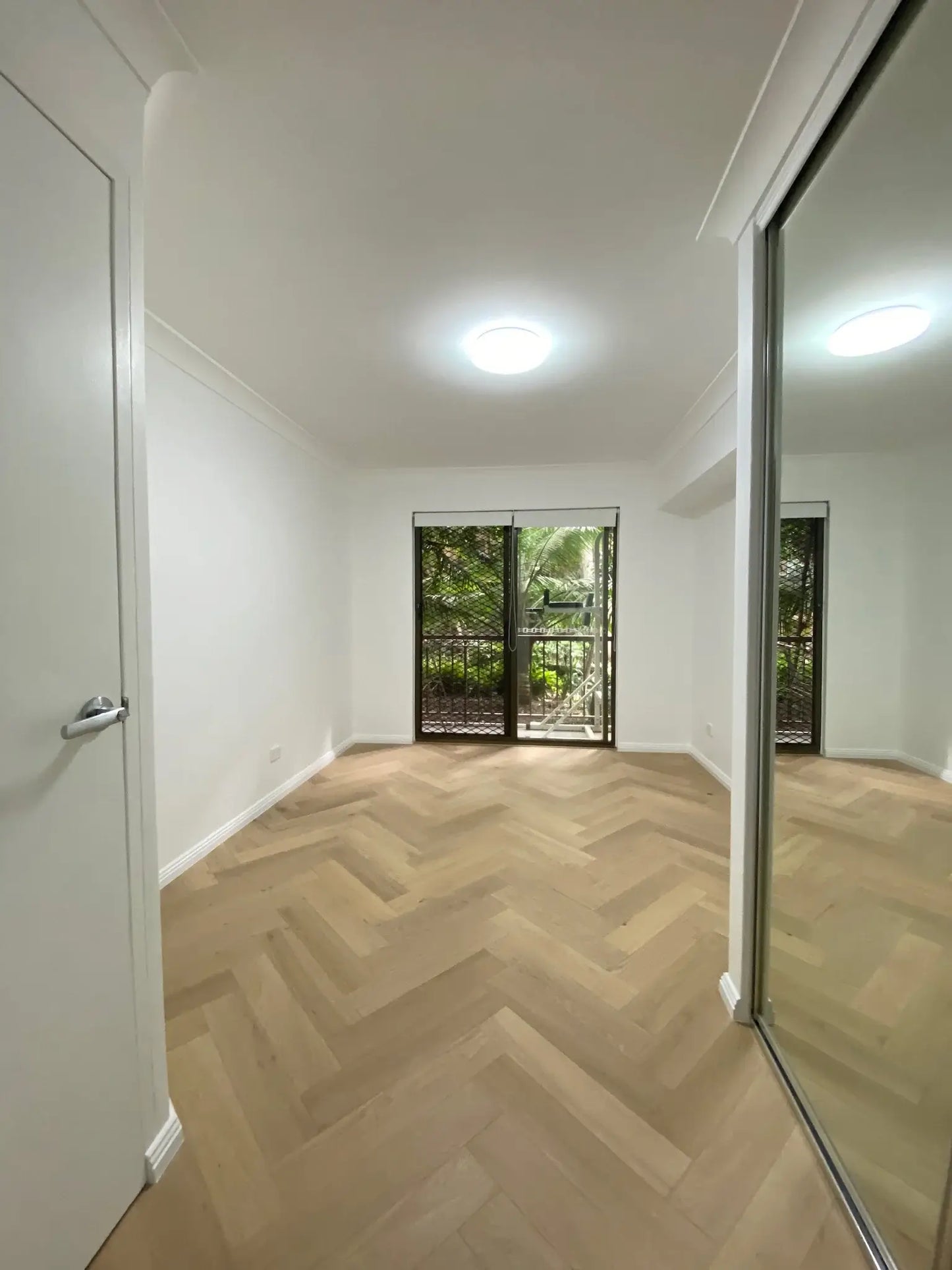 Empty room with wooden floor, white walls, and a door leading to a balcony.