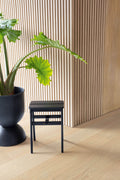 Black stool next to a potted plant against a wooden paneled wall.