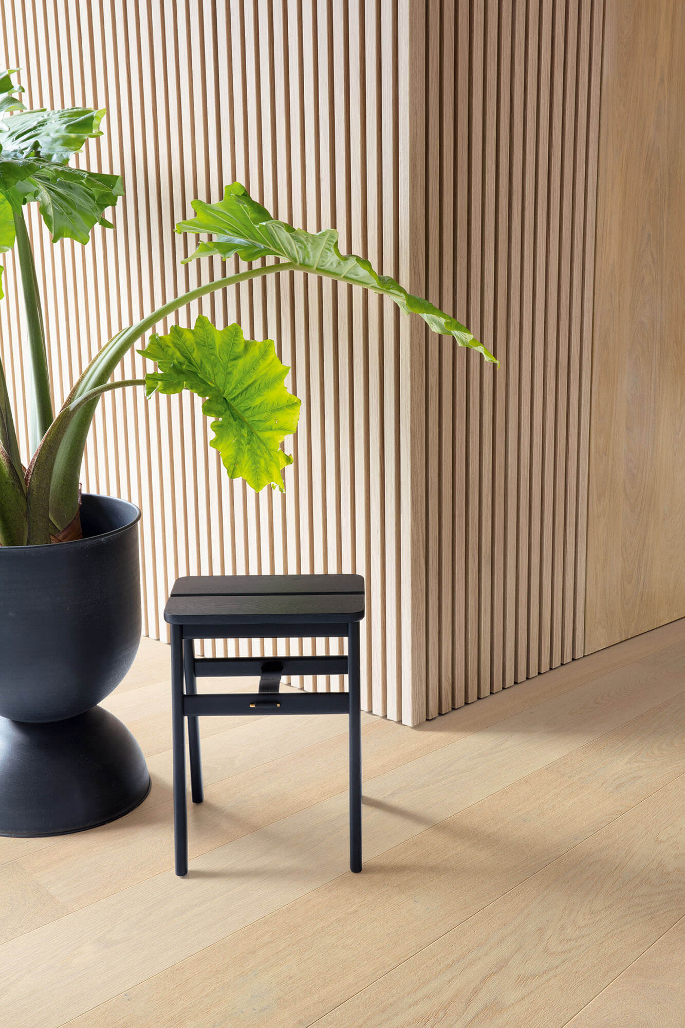 Black stool next to a potted plant against a wooden paneled wall.