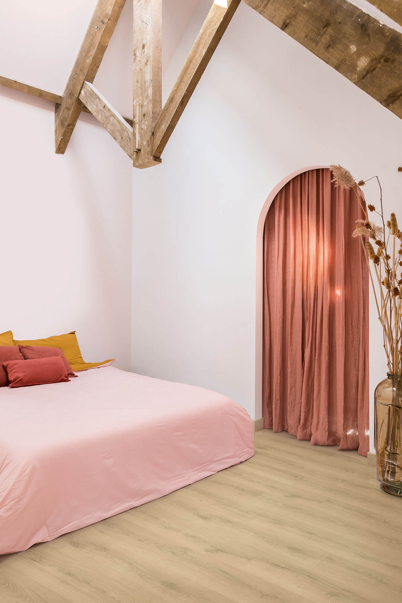 Bedroom with pink bedding, wooden beams, and a pink curtain archway.