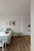 Modern bedroom with a bed, side table, and cat on a wooden floor.