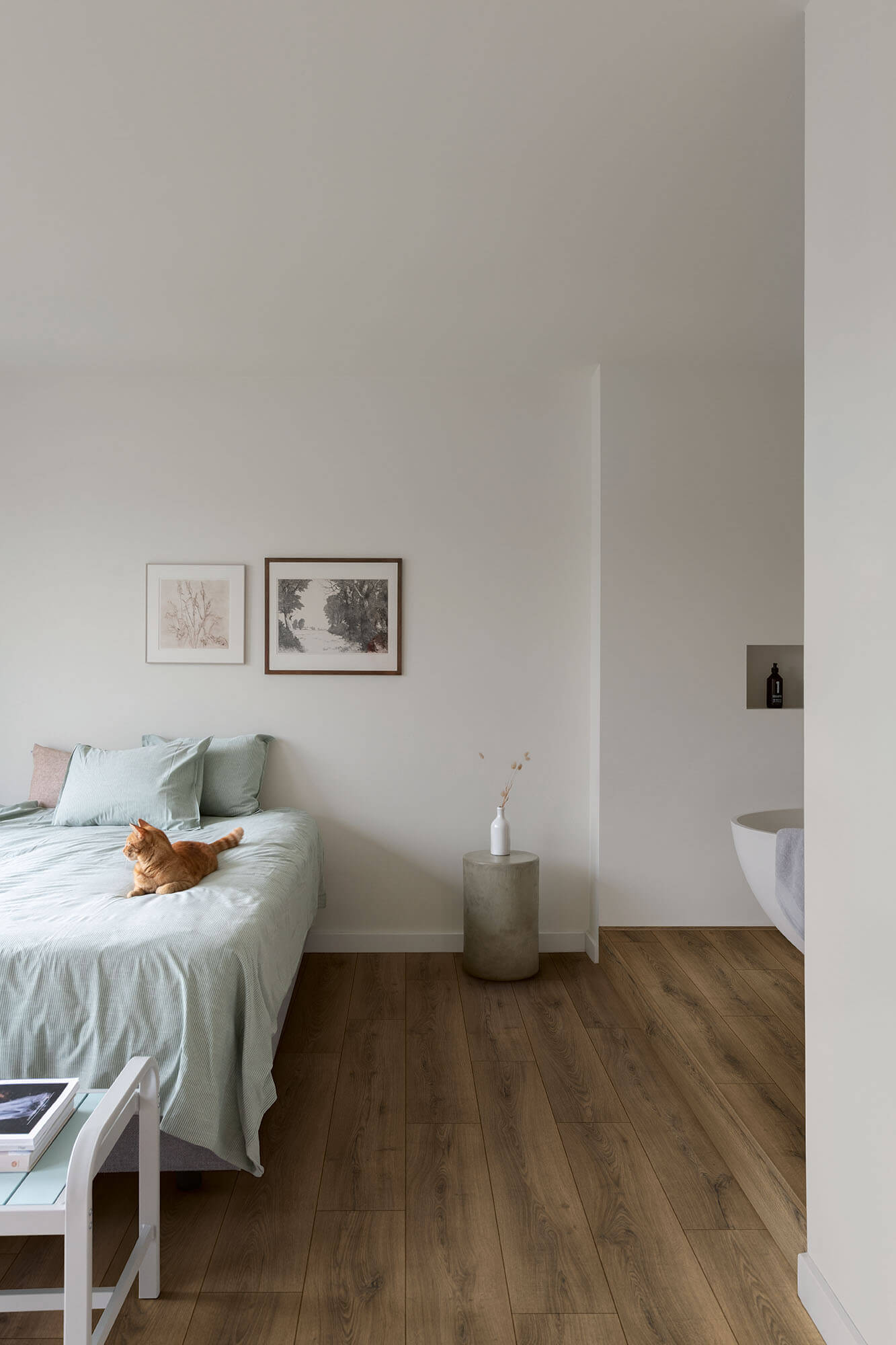 Modern bedroom with a bed, side table, and cat on a wooden floor.